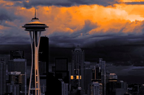 Seattle skyline at sunset, featuring the Space Needle against dramatic clouds and city buildings.