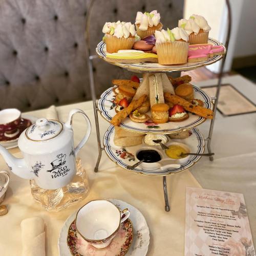 A tiered stand with assorted pastries, sandwiches, and a teapot on a table set for afternoon tea.