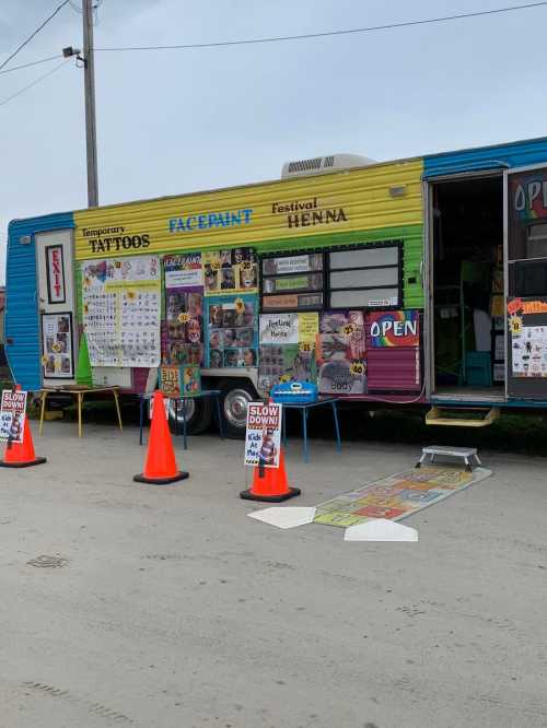 A colorful mobile booth offering tattoos, face paint, and henna, with signs and cones marking the area.