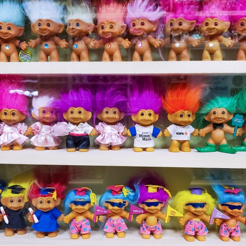 A colorful display of troll dolls with various hairstyles and outfits, arranged on a shelf.