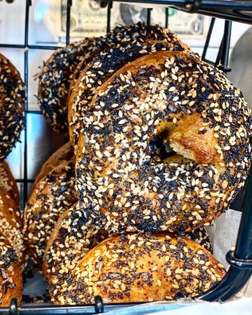 A close-up of a basket filled with sesame-seeded bagels, some with a dark, crispy crust.