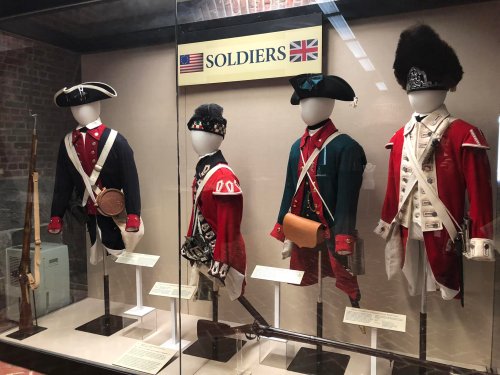 Display of historical soldier uniforms from the American and British sides, featuring mannequins in period attire.