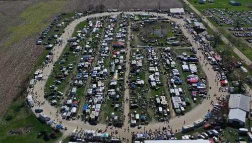 Aerial view of a bustling outdoor market with numerous stalls, vehicles, and crowds in a circular layout.