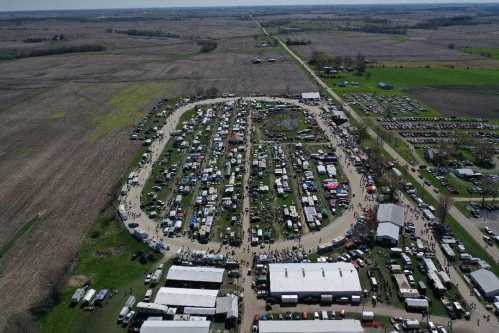 Aerial view of a large outdoor event with numerous tents, vehicles, and crowds in a rural landscape.