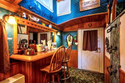 Cozy room with a bar area, wooden stools, blue wallpaper, and a door leading outside. Warm lighting enhances the ambiance.