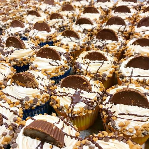 A close-up of rows of cupcakes topped with frosting, chocolate, and a peanut butter cup.