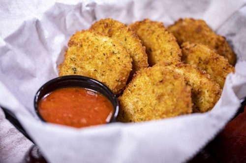 A basket of golden-brown fried food with a side of marinara sauce for dipping.
