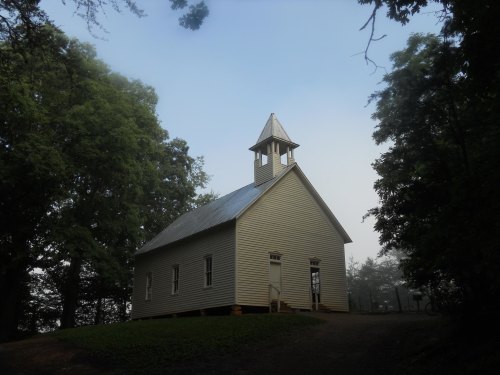 A small, white church with a steeple, surrounded by trees in a misty landscape.