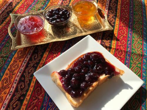 A slice of bread topped with berry jam, accompanied by three small bowls of different jams on a decorative tray.