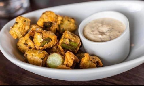 A bowl of crispy fried okra served with a small cup of dipping sauce.