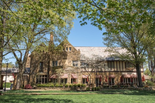 A large stone building with a sloped roof, surrounded by green trees and a manicured lawn on a sunny day.