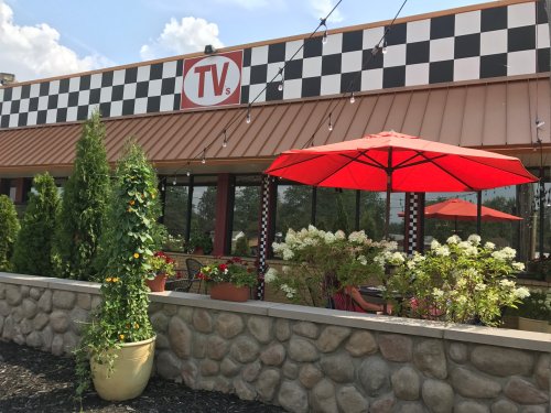 Exterior of a restaurant with a checkered facade, featuring a red umbrella over a patio surrounded by greenery.