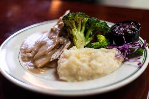 A plate of sliced turkey with gravy, mashed potatoes, steamed broccoli, and a side of cranberry sauce.