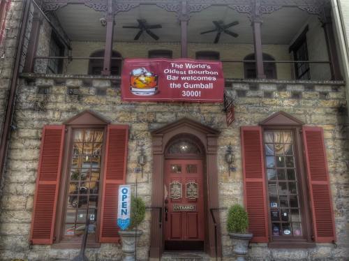 Historic building with stone facade, red shutters, and a sign welcoming the Gumball 3000 event at the oldest bourbon bar.