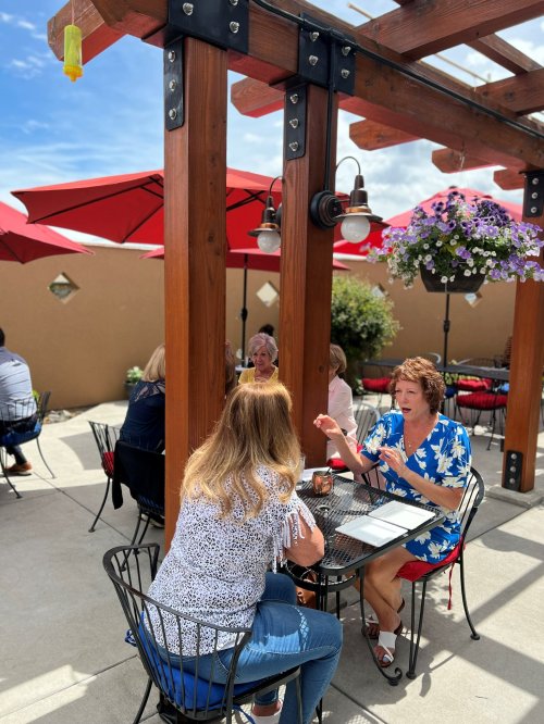 A sunny outdoor restaurant patio with diners seated under red umbrellas, enjoying food and conversation.