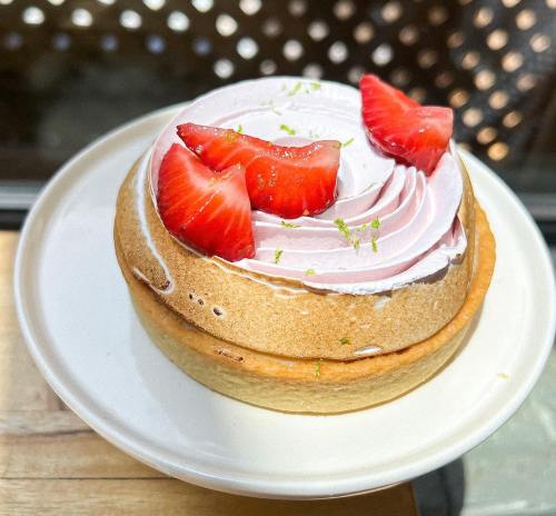 A round dessert with a creamy pink topping, decorated with fresh strawberry slices and a hint of lime zest.