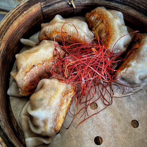 A bamboo steamer filled with dumplings topped with red threads, showcasing a crispy bottom and soft texture.