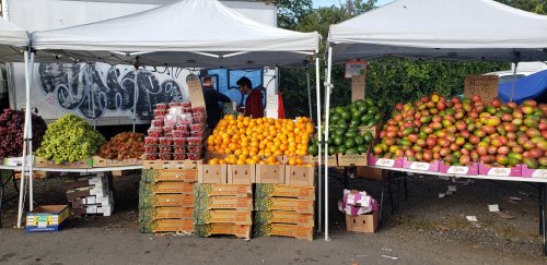 A vibrant outdoor market with tents displaying various fruits, including grapes, oranges, and apples, stacked in boxes.