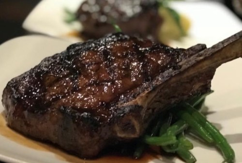 A close-up of a grilled ribeye steak on a plate, garnished with green beans and a rich sauce.