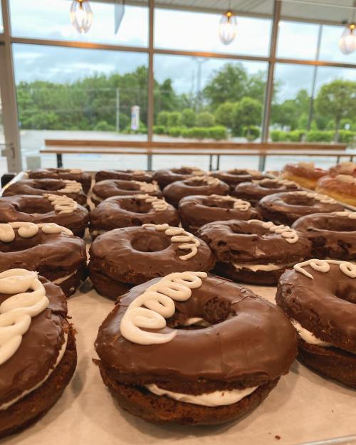 A tray of chocolate-covered donuts filled with cream and topped with white icing, displayed in a bright café setting.