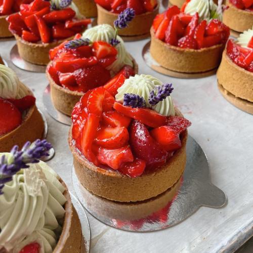 Delicious strawberry tarts topped with cream and lavender, arranged on a silver tray.