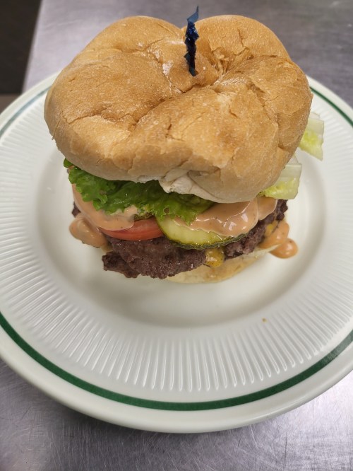 A close-up of a hamburger with lettuce, tomato, pickles, and sauce, served on a plate with a toothpick on top.