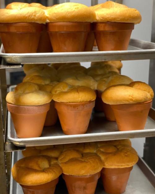 Baked goods resembling fluffy soufflés in terracotta pots, arranged on metal trays.