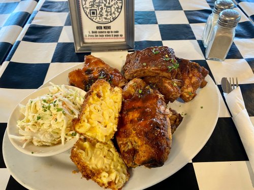 A plate of barbecue ribs with macaroni and cheese, coleslaw, and a QR code menu on a checkered tablecloth.