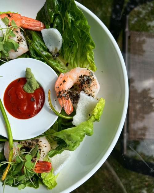 A plate of shrimp on lettuce with a small bowl of sauce and wasabi, garnished with microgreens.