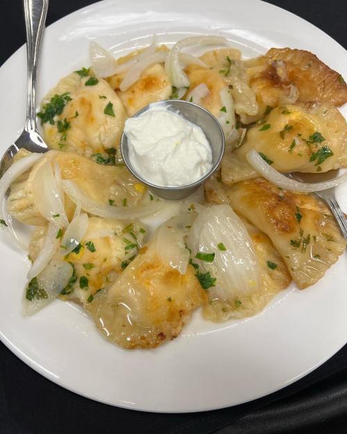 A plate of golden-brown pierogi topped with sautéed onions and served with a side of sour cream.