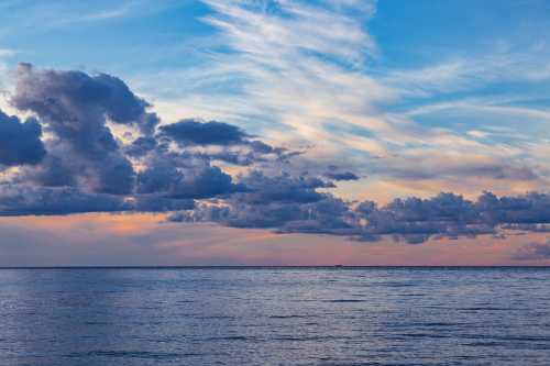 A serene ocean view at sunset, featuring colorful clouds and a calm water surface reflecting the sky.