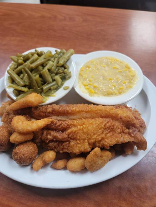 A plate of fried fish with hushpuppies, green beans, and corn pudding on a wooden table.