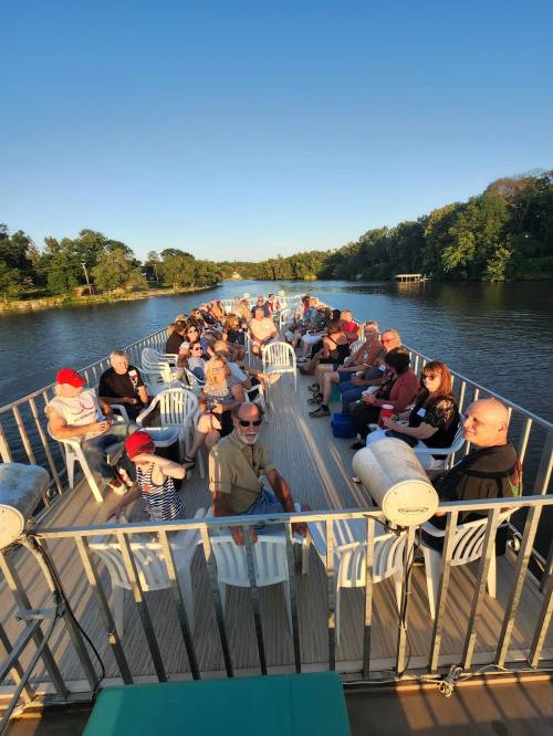 A group of people sitting on a boat, enjoying a scenic view of a river surrounded by trees on a sunny day.