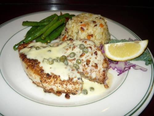 A plate featuring grilled fish with caper sauce, served with rice, green beans, and a lemon wedge.