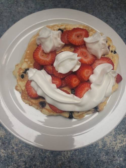 A pancake topped with strawberries and whipped cream arranged to resemble a smiling face.