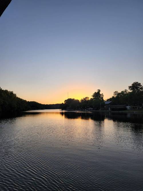 A serene river at sunset, reflecting the colorful sky and surrounded by trees.