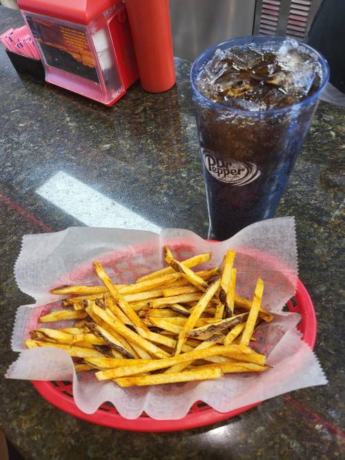 A basket of golden fries on a counter next to a tall cup of iced Dr Pepper.