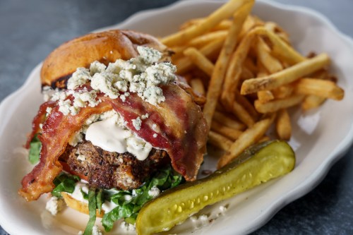 A juicy burger topped with bacon, blue cheese, lettuce, and mayo, served with crispy fries and a pickle on the side.