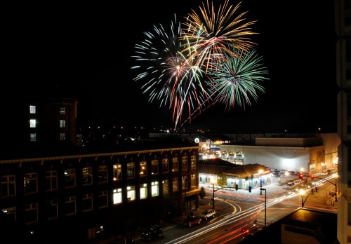 Colorful fireworks illuminate the night sky above a cityscape, with traffic and buildings below.