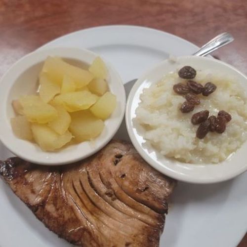A plate with grilled fish, a side of rice topped with raisins, and a bowl of diced pineapple.