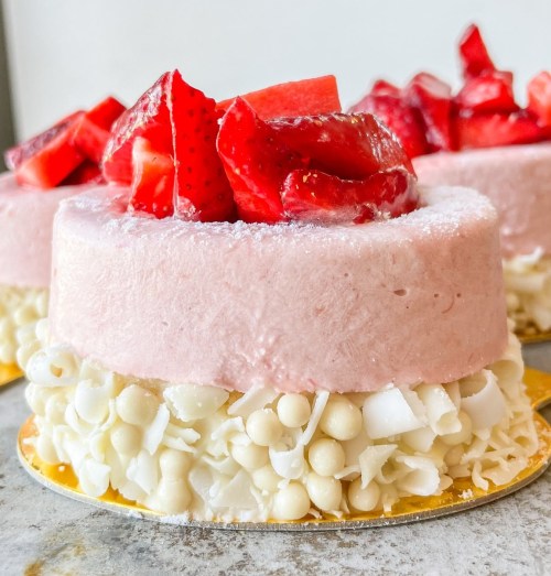 A close-up of a pink mousse cake topped with fresh strawberries and surrounded by white chocolate shavings.