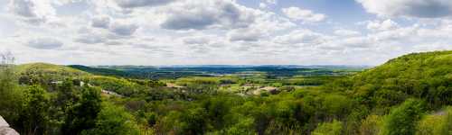 A panoramic view of lush green hills and valleys under a cloudy sky, showcasing vibrant nature in spring.