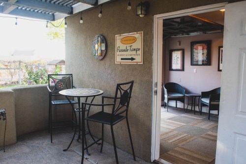 A cozy entrance with a sign pointing to a tasting room, featuring a small table and chairs on a patio.