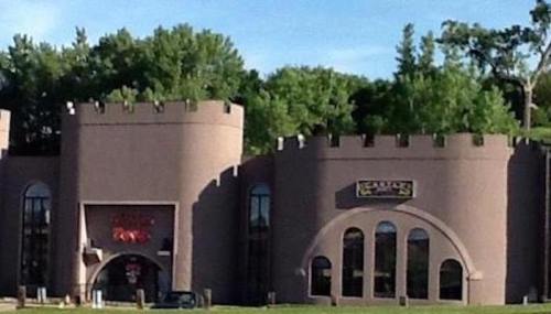 A castle-themed building with turrets and large windows, surrounded by greenery.