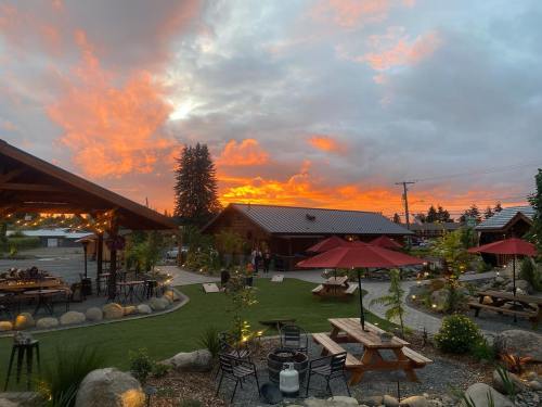 A vibrant sunset casts orange and pink hues over a cozy outdoor dining area with picnic tables and umbrellas.