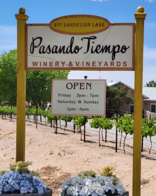 Sign for Pasando Tiempo Winery & Vineyards, listing hours: Fri 3-7pm, Sat & Sun 1-6pm, surrounded by vineyards.