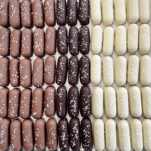 A grid of chocolate-covered candies in dark, milk, and white varieties, sprinkled with coarse salt.
