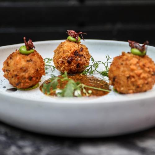Three crispy, golden-brown balls on a plate, garnished with green sauce and herbs.