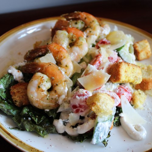 A plate of shrimp salad with lettuce, tomatoes, croutons, and parmesan cheese drizzled with dressing.