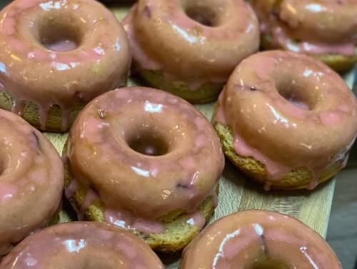 A close-up of freshly baked donuts with pink glaze, arranged on a wooden surface.